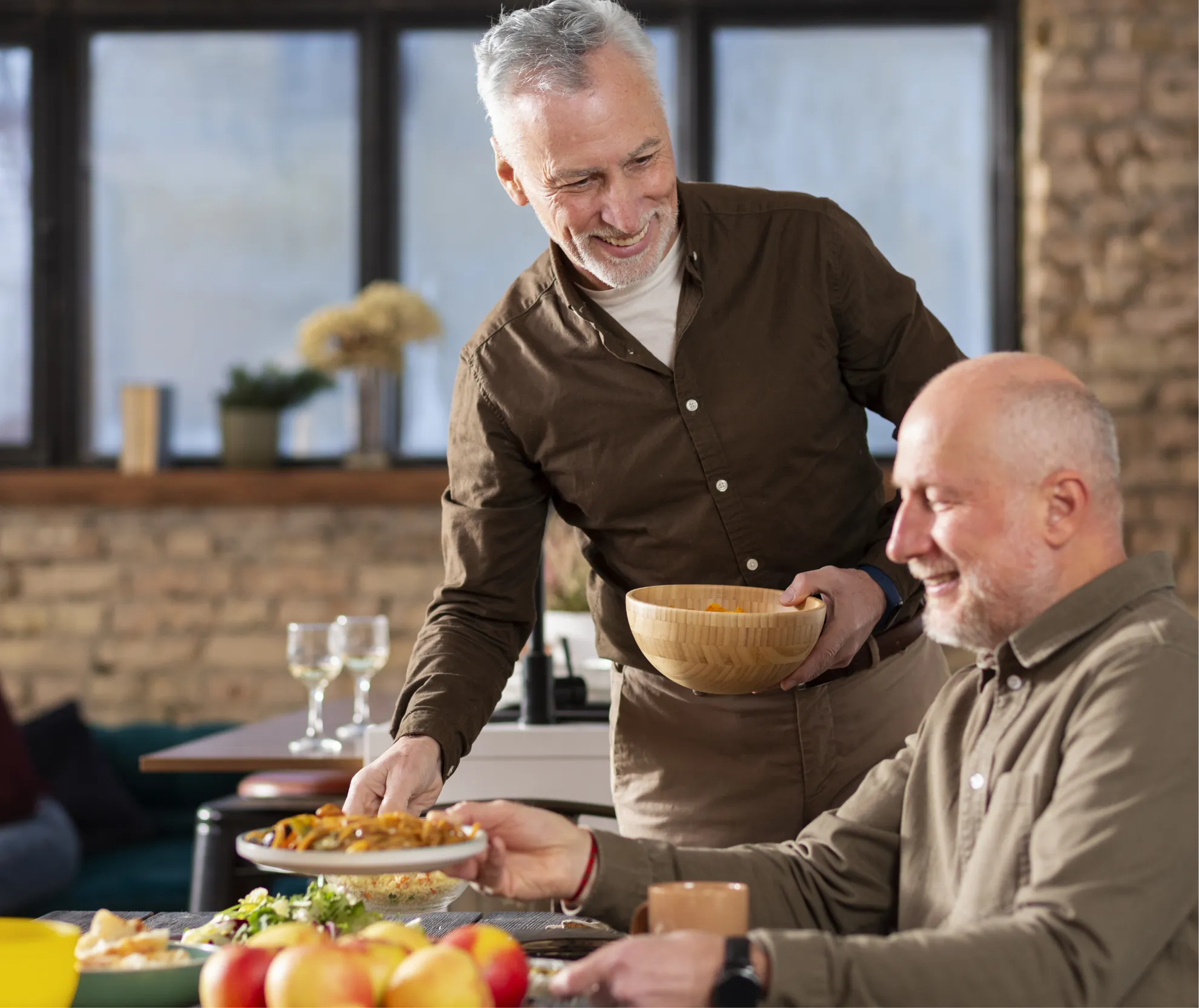 A man serving food to an older man at a table in a cozy dining room setting.